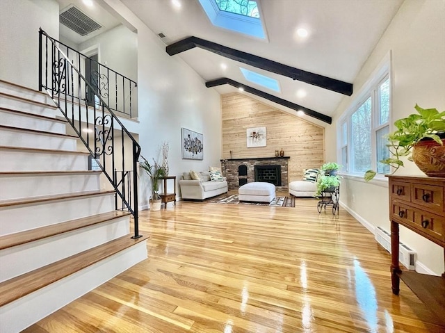 living room with a brick fireplace, hardwood / wood-style floors, beam ceiling, a skylight, and baseboard heating