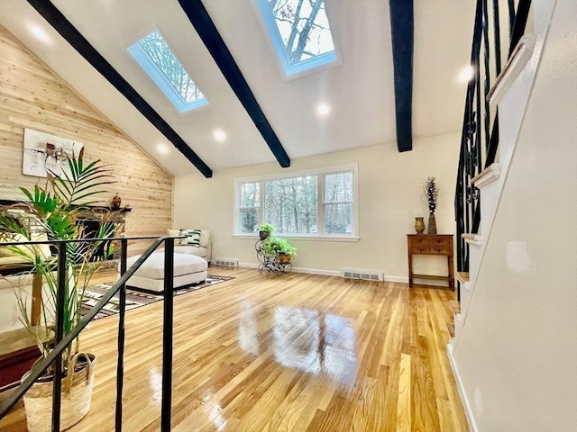 workout area featuring high vaulted ceiling, light wood-type flooring, a skylight, and wooden walls