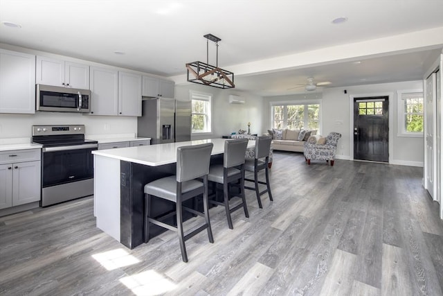 kitchen with gray cabinets, appliances with stainless steel finishes, hanging light fixtures, a center island, and light hardwood / wood-style floors