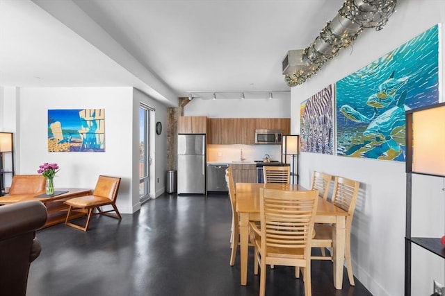 dining area featuring baseboards, rail lighting, and finished concrete floors