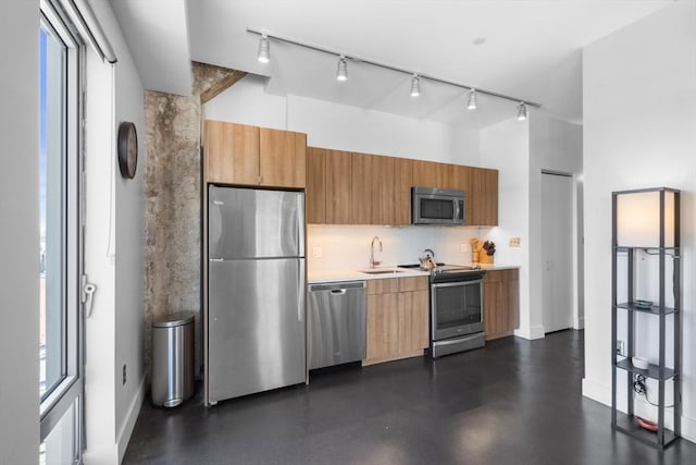 kitchen with backsplash, a sink, light countertops, track lighting, and stainless steel appliances