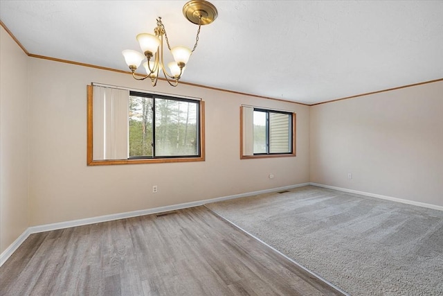 empty room featuring a chandelier, crown molding, and baseboards