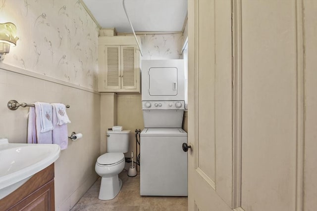 bathroom with vanity, toilet, stacked washer / dryer, and wallpapered walls