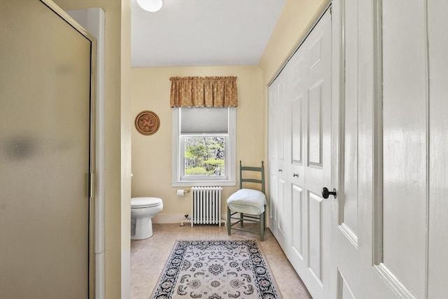 bathroom with radiator, a shower with shower door, toilet, and baseboards