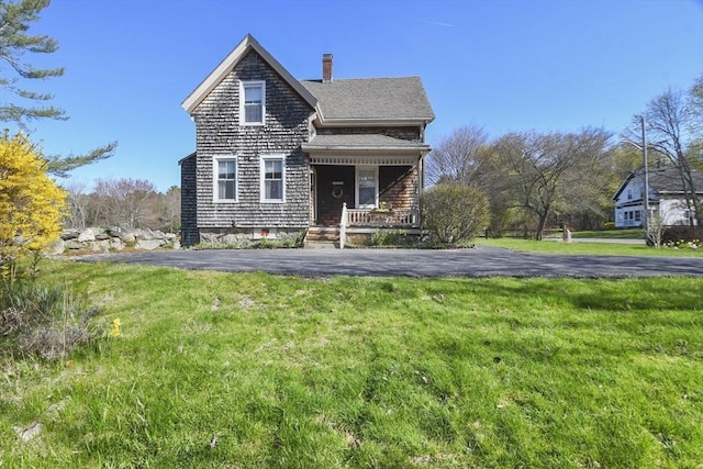 view of front of home with a chimney, a front lawn, a shingled roof, and covered porch