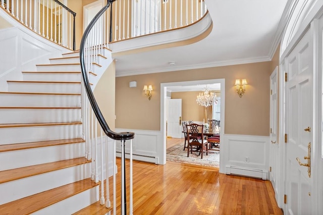 entrance foyer featuring a baseboard radiator, ornamental molding, an inviting chandelier, and light wood-type flooring