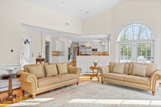 living room with high vaulted ceiling, light wood-type flooring, a chandelier, and baseboard heating