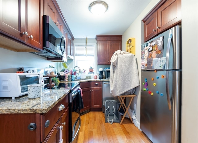 kitchen with light wood-type flooring, light stone counters, appliances with stainless steel finishes, and sink