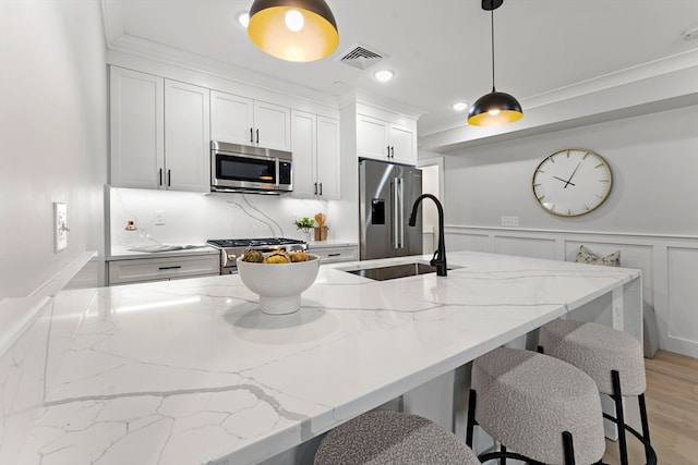 kitchen with white cabinets, hanging light fixtures, light hardwood / wood-style flooring, stainless steel appliances, and light stone countertops