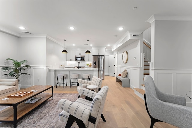 living room featuring light wood-type flooring, ornamental molding, and sink