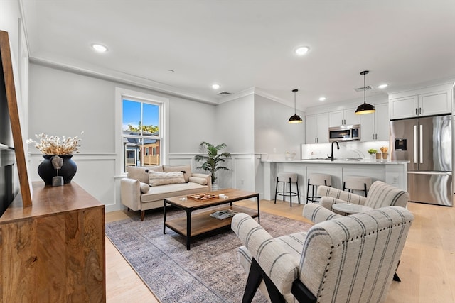 living room with light hardwood / wood-style floors, sink, and crown molding