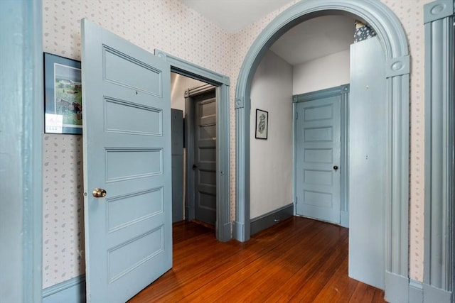 hall with dark wood-style flooring, wallpapered walls, baseboards, and arched walkways