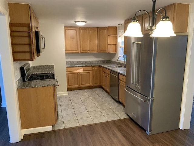 kitchen with sink, hanging light fixtures, dark stone countertops, light wood-type flooring, and appliances with stainless steel finishes