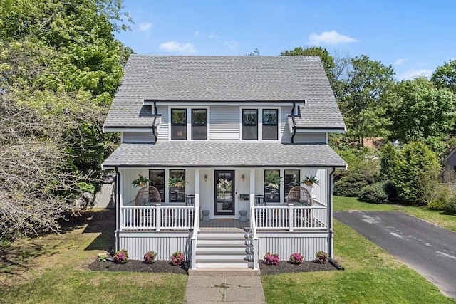 view of front of property with a porch, roof with shingles, and a front yard