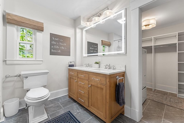 bathroom featuring baseboards, double vanity, and toilet