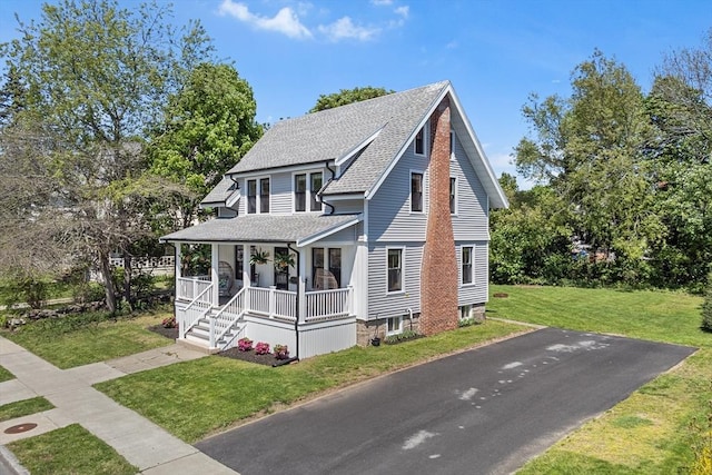 view of front of home featuring a porch, roof with shingles, and a front yard