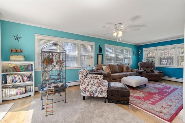 living area with a ceiling fan, a baseboard heating unit, a wealth of natural light, and wood finished floors