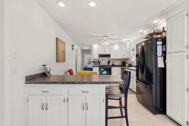 kitchen with white cabinets, a peninsula, light tile patterned flooring, and black appliances