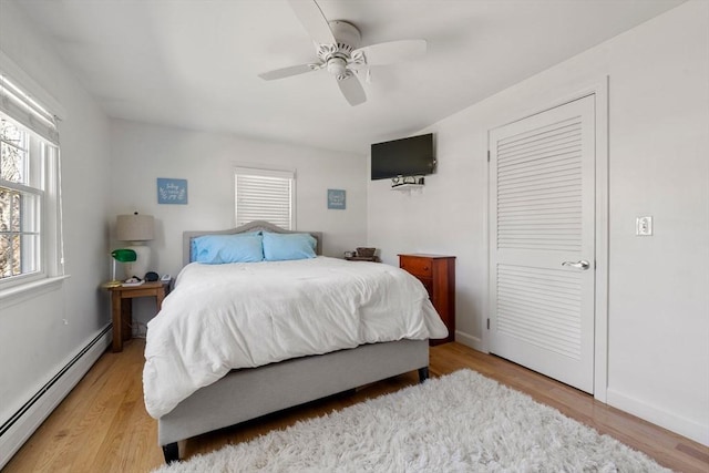 bedroom featuring light wood-style floors, a closet, baseboard heating, and a ceiling fan