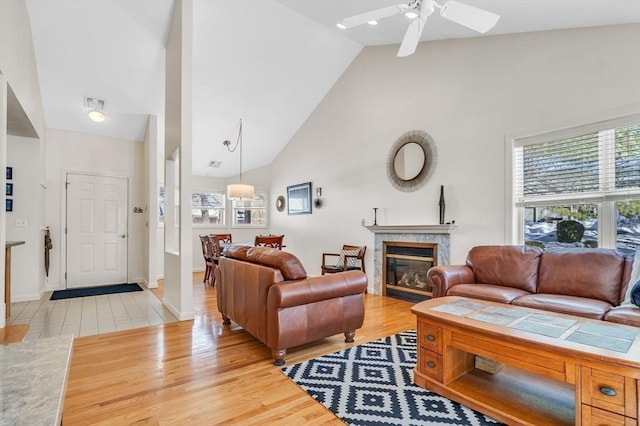 living area with visible vents, a premium fireplace, light wood-style floors, high vaulted ceiling, and baseboards