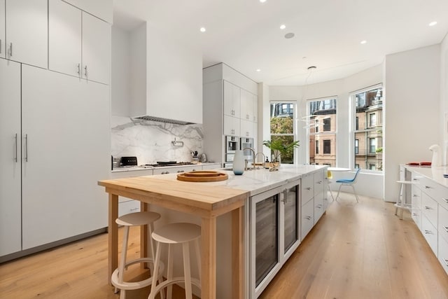 kitchen with backsplash, light hardwood / wood-style floors, white cabinetry, a kitchen bar, and a center island with sink