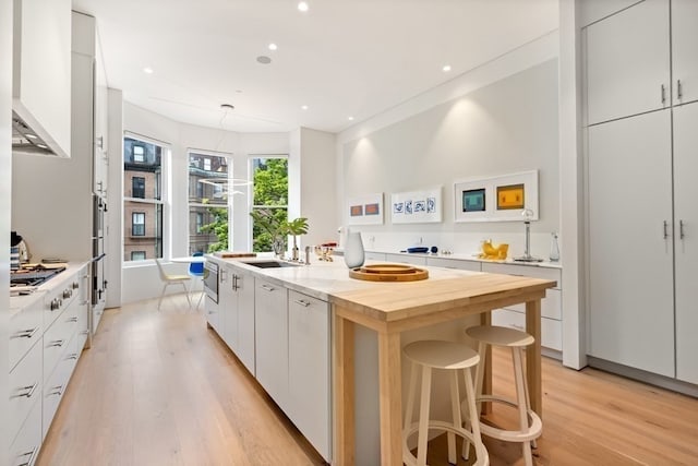 kitchen featuring a breakfast bar area, a center island with sink, light hardwood / wood-style flooring, custom range hood, and white cabinetry