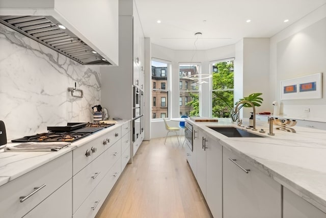 kitchen featuring light wood-type flooring, custom exhaust hood, backsplash, light stone counters, and sink