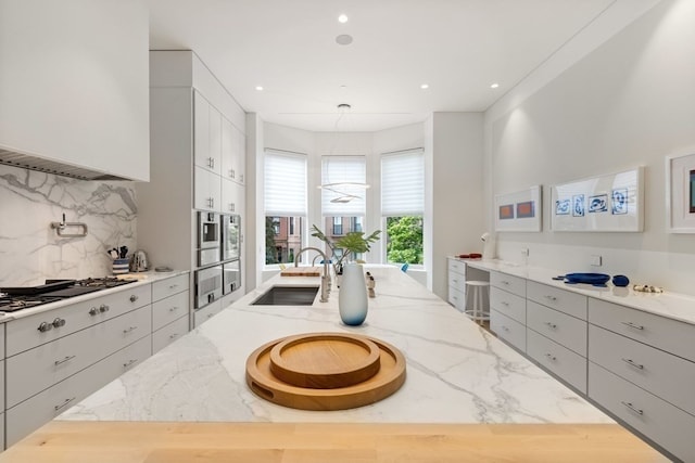 interior space featuring ventilation hood, light stone counters, stainless steel appliances, sink, and decorative backsplash