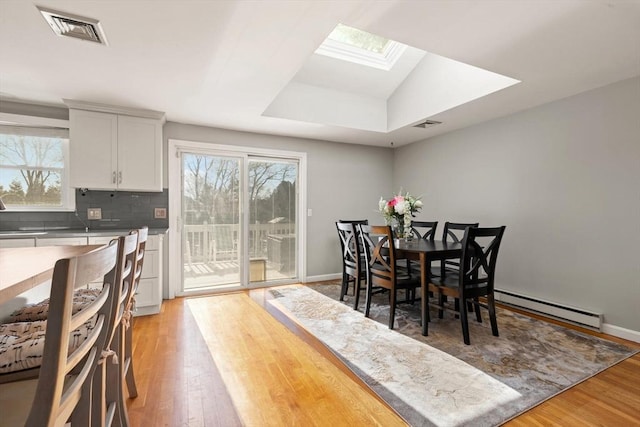 dining area featuring light wood-type flooring, vaulted ceiling with skylight, and baseboard heating