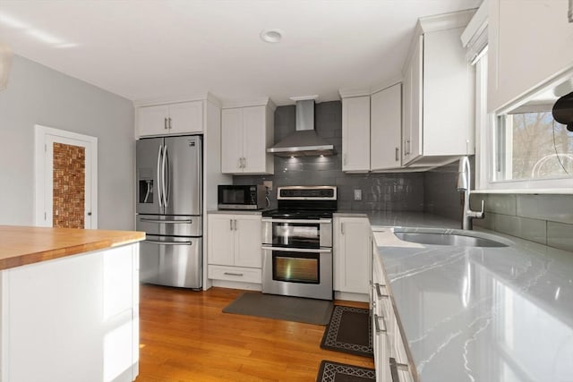 kitchen with appliances with stainless steel finishes, sink, white cabinets, and wall chimney exhaust hood