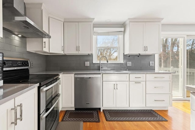 kitchen with white cabinetry, stainless steel appliances, light hardwood / wood-style floors, and wall chimney range hood