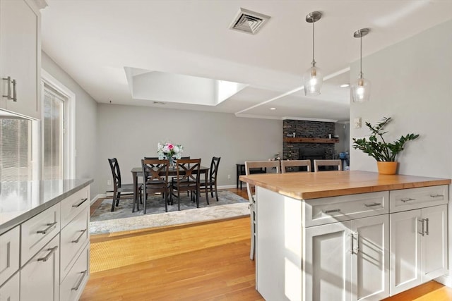 kitchen featuring pendant lighting, wooden counters, a fireplace, and white cabinets