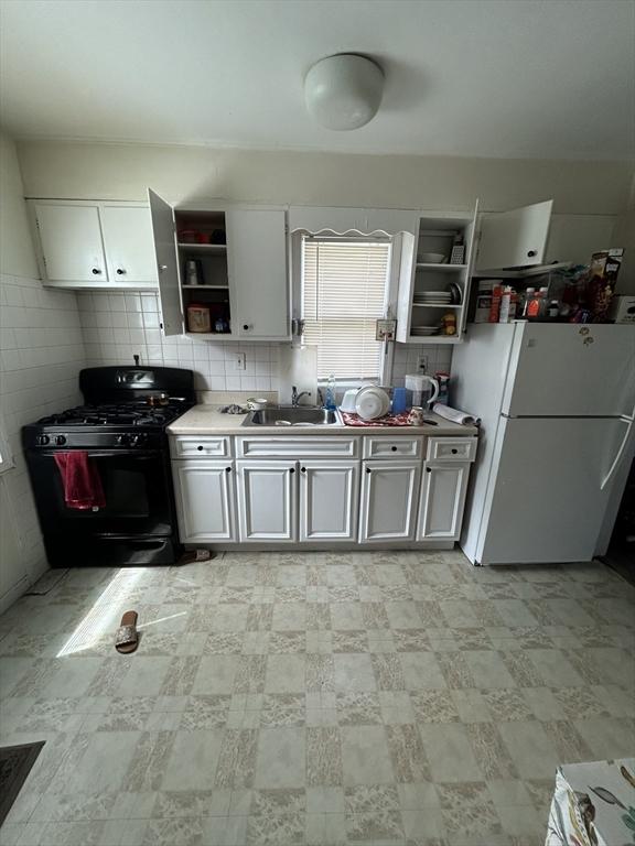 kitchen featuring black gas range, white cabinetry, sink, backsplash, and white fridge