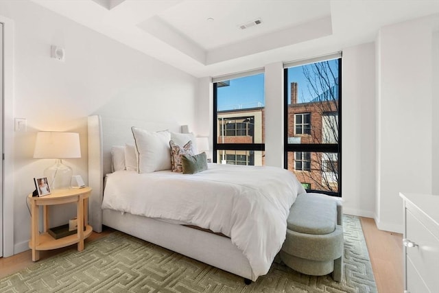 bedroom with a tray ceiling, visible vents, baseboards, and multiple windows