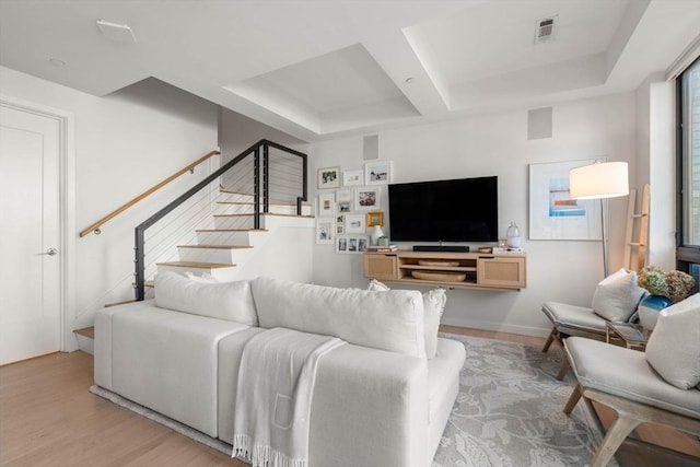 living area with light wood finished floors, visible vents, coffered ceiling, baseboards, and stairs