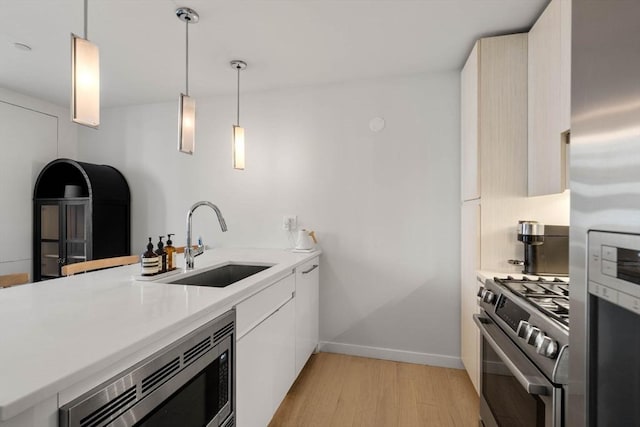 kitchen featuring light countertops, appliances with stainless steel finishes, a sink, modern cabinets, and light wood-type flooring