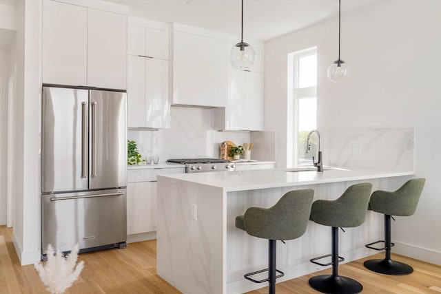 kitchen featuring high quality fridge, white cabinets, sink, decorative light fixtures, and light hardwood / wood-style flooring