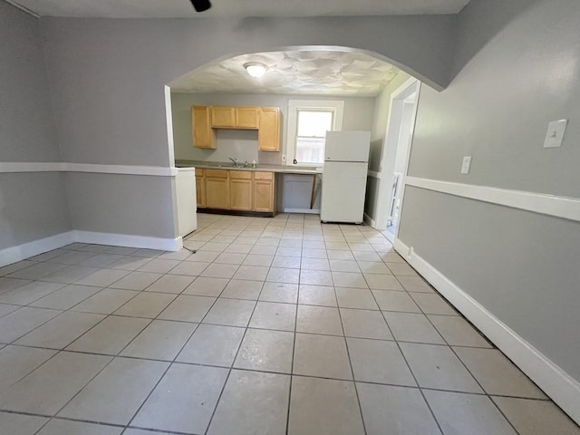 kitchen featuring light countertops, light brown cabinetry, freestanding refrigerator, light tile patterned flooring, and a sink