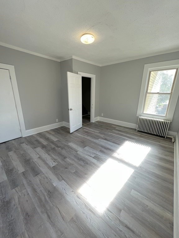 unfurnished bedroom featuring a textured ceiling, wood finished floors, baseboards, radiator, and crown molding