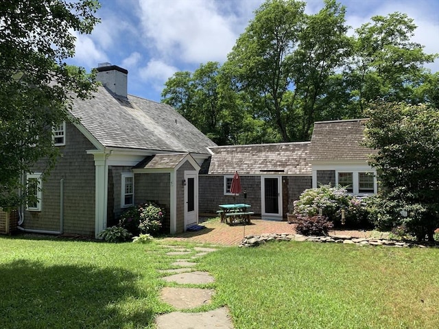 back of house with a patio area, a chimney, a lawn, and roof with shingles