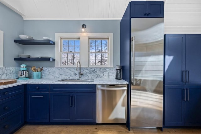 kitchen with blue cabinets, wood finished floors, a sink, appliances with stainless steel finishes, and light stone countertops