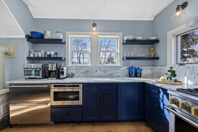 kitchen featuring a toaster, open shelves, stainless steel appliances, light stone countertops, and blue cabinets