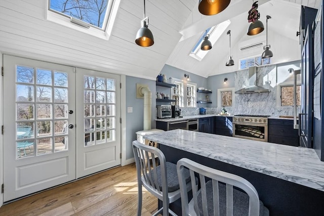 kitchen with high end stove, wall chimney exhaust hood, light wood-type flooring, light stone countertops, and open shelves