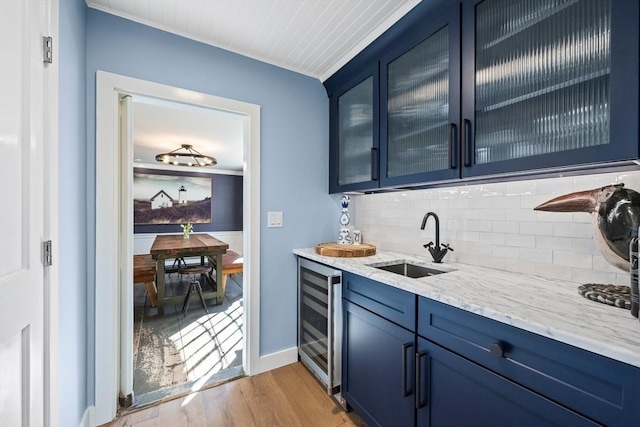 bar featuring beverage cooler, a sink, baseboards, light wood-type flooring, and tasteful backsplash