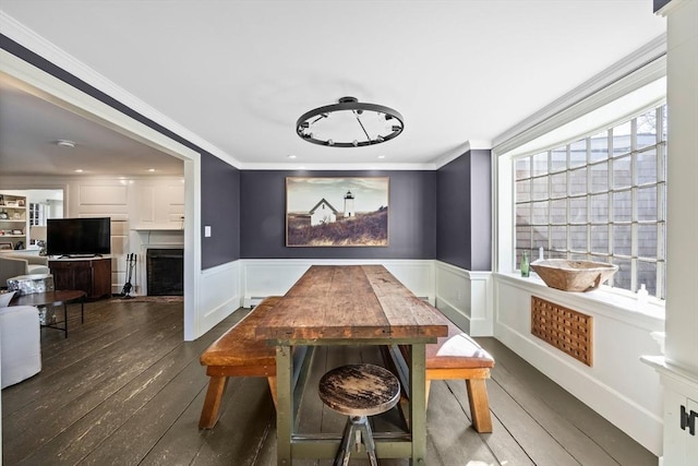 dining room with wainscoting, dark wood-style flooring, crown molding, a healthy amount of sunlight, and a fireplace