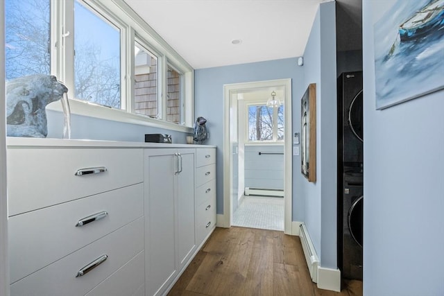 doorway to outside with baseboards, stacked washer / dryer, a baseboard radiator, dark wood-type flooring, and baseboard heating