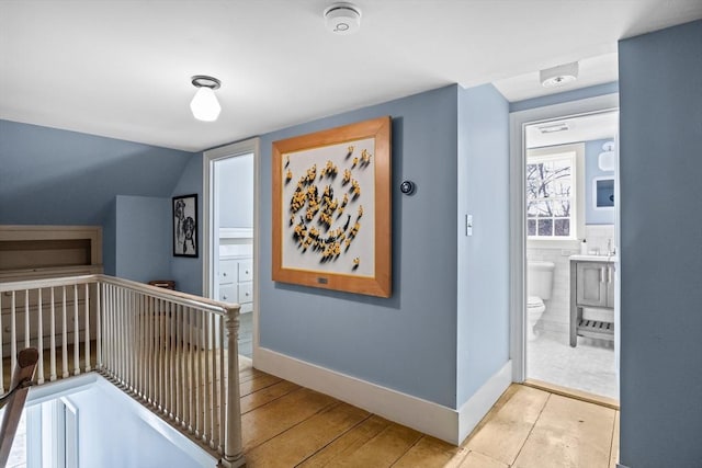 hall featuring tile walls, baseboards, light wood finished floors, and an upstairs landing