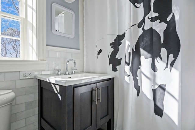 bathroom featuring toilet, wainscoting, vanity, and tile walls