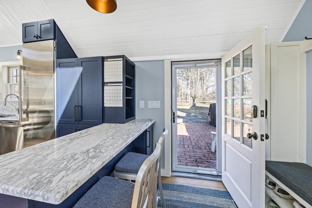 kitchen featuring lofted ceiling, a breakfast bar, wood finished floors, light stone countertops, and a sink