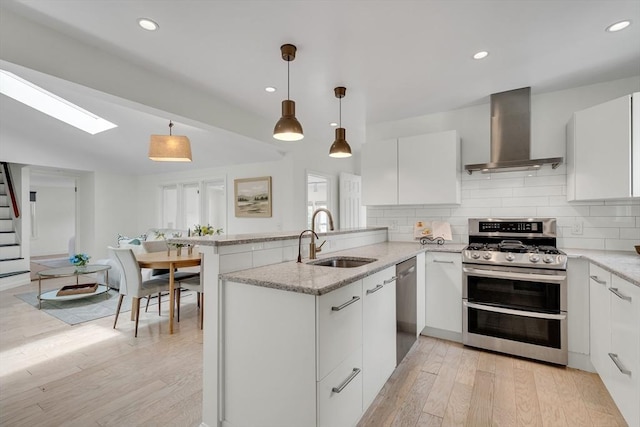 215 Norfolk St Unit 2, Cambridge, MA 02139 - kitchen featuring wall chimney exhaust hood, stainless steel appliances, a peninsula, light wood-style floors, and white cabinetry